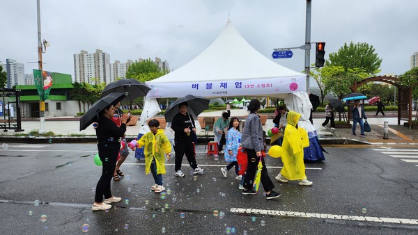 비오는 축제날, 시민들이 차 없는 거리에서 우산과 우비를 쓰고 버블체험을 하고 있다
